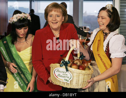 Angela Merkel (C) hält einen Korb mit Äpfeln, die ihr durch die sächsischen Blossom Königin Sina Stegemann (L) und die Lake Constance Apple Queen Ann-Kathrin Wirth (R) vor einer Kabinettssitzung im Kanzleramt in Berlin Mittwoch, 5. Dezember 2007 vorgestellt. Im Dezember präsentiert die zentralen Marketing Organisation von deutschen landwirtschaftlichen Industrien (CMA) traditionell die Mitglieder des Fahrerhauses Stockfoto