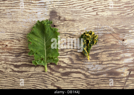 Grünkohl-Blatt neben einem Grünkohl Chip auf verwittertem Holz Stockfoto
