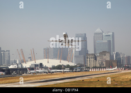 Ein Passagier-Jet hebt ab vom London City Airport mit Canary Wharf und den Millennium Dome im Hintergrund Stockfoto