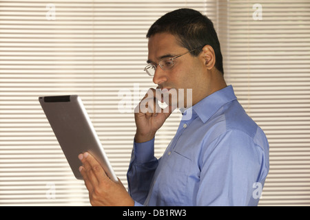 Asiatische Geschäftsmann mit Handy Ipad Tablet-Gerät in der Office-Umgebung, neben Fenster betrachten Stockfoto