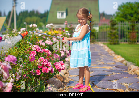 Kleine süße Mädchen Blumen mit einem Schlauch in ihrem Garten gießen Stockfoto