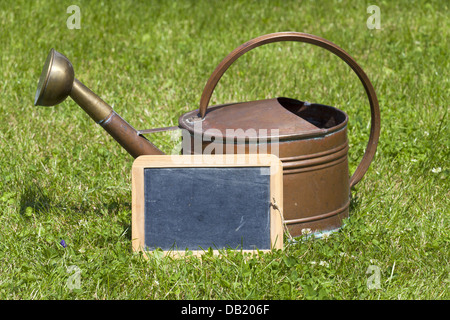 Alte Kupfer Gießkanne und ein unbeschriebenes Blatt, stehend auf dem grünen Rasen Stockfoto