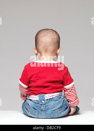 Baby sitzt mit dem Rücken zur Kamera auf grauem Hintergrund isoliert Stockfoto