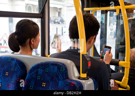 Zwei Menschen sitzen auf einem Londoner Bus Spiel Candy Crush Saga auf ihren Iphones, London, England Stockfoto
