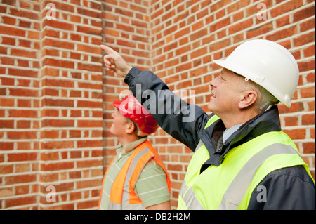 Zwei Bauarbeiter gehen über ihre Pflichten. Bauleiter mit ein allgemeine Arbeiter, sowohl reden und diskutieren den Job. Stockfoto