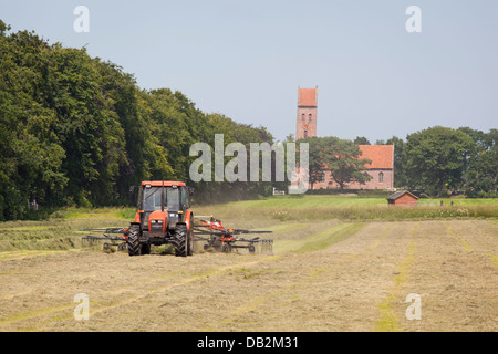 Heuernte mit einem Traktor in Midwolde (Groningen) mit der alten Kirche von Midwolde im Hintergrund Stockfoto
