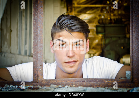 Attraktive Jüngling am rostigen Fenster mit lustigen Ausdruck auf seinem Gesicht, auf der Suche in der Kamera Stockfoto