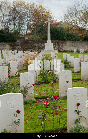 Reihen von weißen eingeschrieben Grundsteine auf kriegsgräber (mit roter Rose) & Kreuz des Opfers jenseits - Stonefall Friedhof, Harrogate, Yorkshire, England, UK. Stockfoto