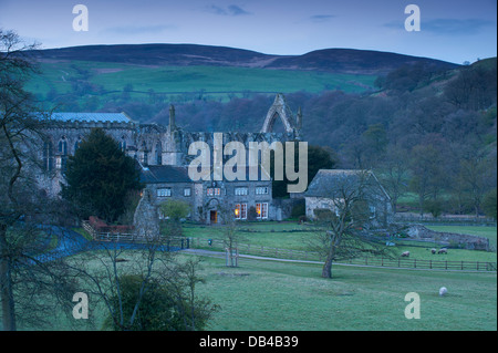 Malerische Aussicht über Bolton Abbey unter Hügeln in ländlichen Tal bei Dämmerung eingebettet, mit goldenen Glanz der Lichter im Alten Pfarrhaus - Yorkshire Dales, England, UK. Stockfoto