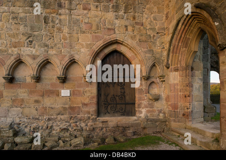 Serie von Steinmetzbögen an der Wand, geschlossene Holztür und gewölbter Türeingang zu den historischen Ruinen der Bolton Abbey, Yorkshire Dales, England, Großbritannien. Stockfoto