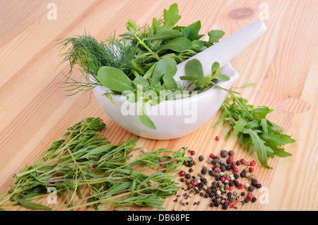 Mörtel mit Farbe Pfeffer, frischer Feldsalat, Rucola, Thymian, Majoran und Dill auf Holzbrett Stockfoto