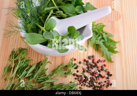 Mörtel mit Farbe Pfeffer, frischer Feldsalat, Rucola, Thymian, Majoran und Dill auf Holzbrett Stockfoto