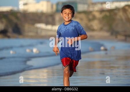 Kleiner Junge spielt und läuft in der Brandung entlang einer englischen Strand bei Sonnenuntergang Stockfoto