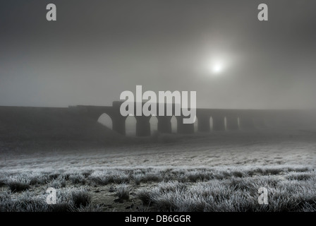 Die ribblehead Viadukt im Winter mit Bahnübergang und Sonne durch Nebel bilden ein stimmungsvolles Bild. Stockfoto
