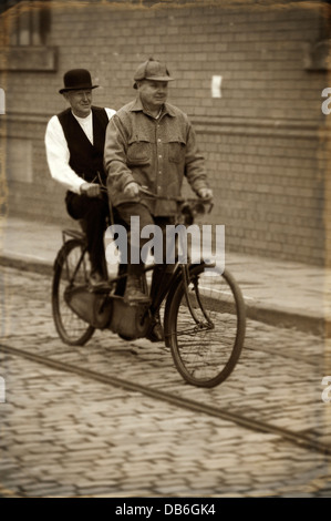 zwei edwardian Männer, die mit dem Tandem-Fahrrad auf einer gepflasterten Straße Stockfoto