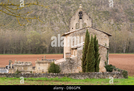 Ländliche Kirche Frühling Felder. Eine alte steinerne Kirche und Friedhof inmitten eines neu gepflügtes Feld der roten Erde. Tarn, Frankreich Stockfoto