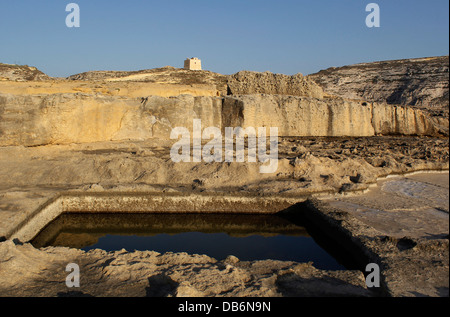 Blick über ein traditionelles Salz Pan im Rock in Richtung Img Dwejra Tower manchmal als Qawra Tower einen kleinen Wachturm in Dwejra Bay auf der Insel Gozo in Malta bekannt geschnitzt Stockfoto