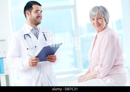 Zuversichtlich Arzt mit Stethoskop und Zwischenablage Blick auf seinen älteren Patienten Stockfoto