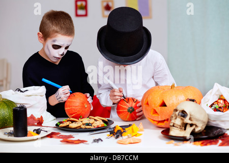 Foto von zwei unheimlichen jungen Zeichnung auf Kürbisse an Halloween Tisch Stockfoto