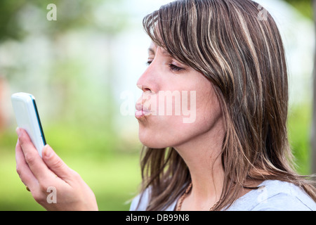 Kaukasische junge Frau, die versucht, Outdoor-Handy zu küssen Stockfoto