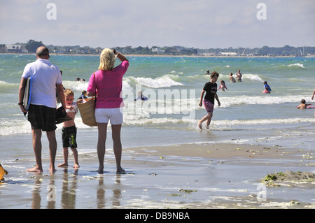 Paar mit Enkelkind an sonnigen West Wittering blaue Flagge Strand nr. Chichester, West Sussex, UK mit Hayling Island in Ferne Stockfoto