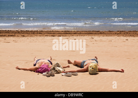 Zwei Frauen mit überdachten Köpfe spreadeagle am Strand Sonnenbaden. Stockfoto