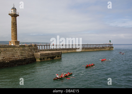 Ruderboot-Rennen im Hafen von Whitby mit der West Pier und Leuchttürme im Hintergrund Stockfoto