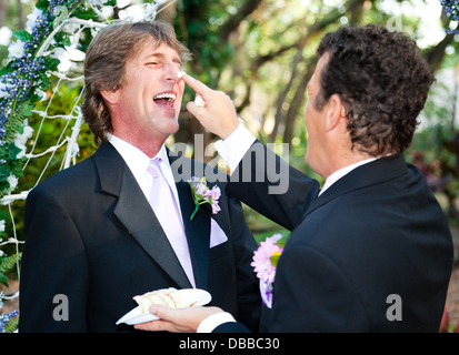 Ein Bräutigam setzt spielerisch Hochzeitstorte auf seinem Mann Nase bei ihrer Hochzeit. Stockfoto