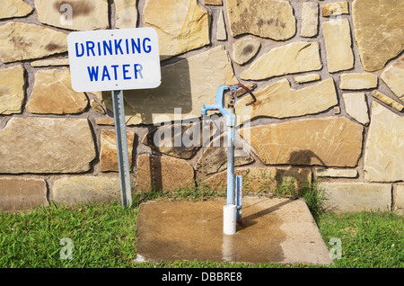 Trinkwasserhahn mit Zeichen und fließendem Wasser hinter einer Steinmauer Stockfoto