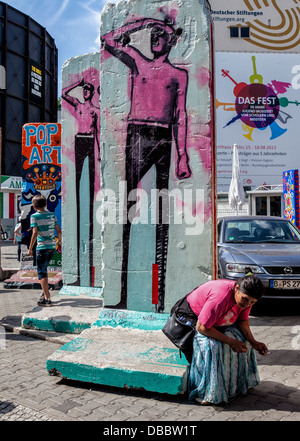 Frau sitzt auf Basis des gemalten Fragment der Berliner Mauer am Checkpoint Charlie Border Post, Cheeseburger, Berlin Stockfoto