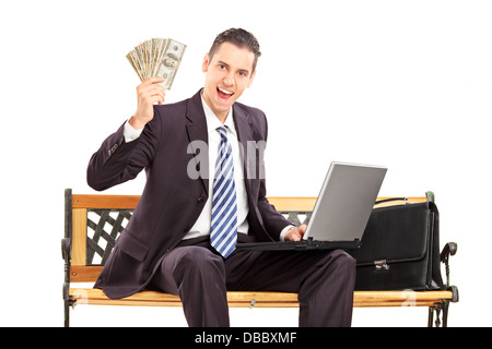 Glücklich Kaufmann mit Laptop sitzt auf einer Holzbank und hält US-Dollar Stockfoto
