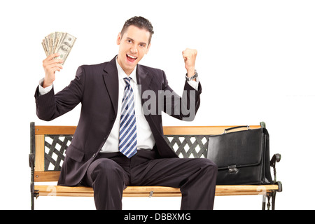 Glücklich Kaufmann im schwarzen Anzug sitzt auf einer Holzbank und hält US-Dollar Stockfoto