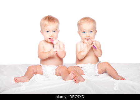 Zwei niedliche adorable Baby Babys mit blauen Augen sitzen und Löffel essen, spielen, auf weiß.