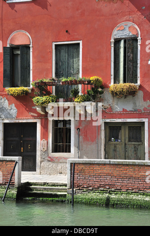 Venezianischen Haus am Kanal Seite bemalt rot Ocker mit grünen Fensterläden und Türen und Blumen bedeckt Balkon, Venedig, Italien Stockfoto