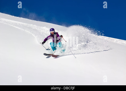 Frau Skifahrer an einem steilen Berghang. Im Gegenzug wirft den Schnee Staub. Stockfoto