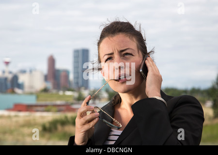 Seriöse Geschäftsfrau mit iPhone im Freien mit Downtown City Skyline im Hintergrund Stockfoto