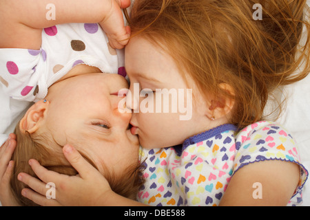 Ältere Schwester küssen Baby im Bett Stockfoto