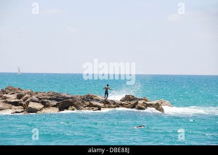 Ein Junge steht Man auf dem Steg als Wellen des Mittelmeers Absturzes auf den Felsen in der Strand von Tel Aviv, Israel Stockfoto