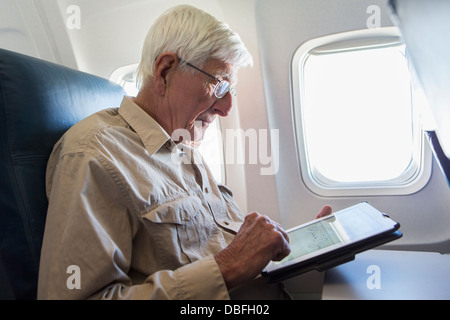 Älteren kaukasischen Mann mit Tablet-PC auf Flugzeug Stockfoto