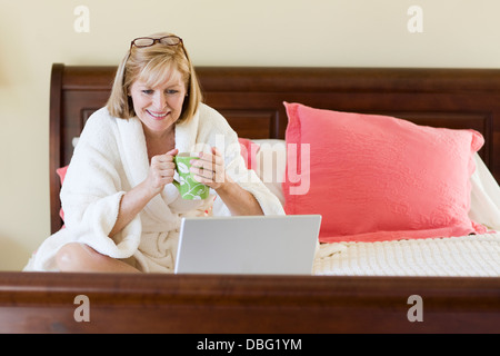 Kaukasische Frau mit Laptop am Bett Stockfoto