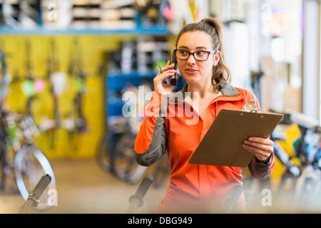 Kaukasische Frau am Telefon im Fahrradgeschäft Stockfoto