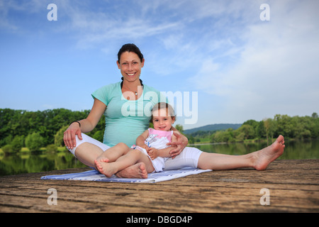 Schwangere Frau und ihre kleine Tochter machen Yogaübung am See Stockfoto