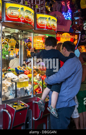 Vater mit Sohn betrachten Greifer-Kran-Spiel-Maschine gefüllt mit Spielzeug in Spielhalle auf Reisen Kirmes / fun fair Karneval Stockfoto