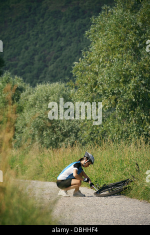 junge Frau mit Mountainbike training und Reparatur Plattfuß auf der Strecke in Landschaft Stockfoto