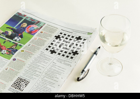 The Times Zeitung öffnen um die kryptische Kreuzworträtsel-Seite mit einem Stift und einem Glas Weißwein daneben. Stockfoto