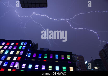 Blitze durchziehen den Himmel bei einem Gewitter in der Nacht, gesehen über den bunt beleuchteten Fenstern eines Designhotels im Chaoyang-Viertel von Peking, China. © Olli Geibel Stockfoto