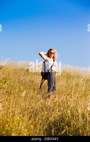 Teenager-Mädchen zu Fuß durch eine Wiese mit einer Gitarre. Im Freien. Sommer. Stockfoto