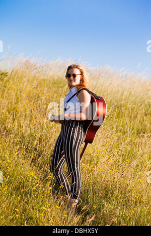 Teenager-Mädchen zu Fuß durch eine Wiese mit einer Gitarre. Im Freien. Sommer. Stockfoto