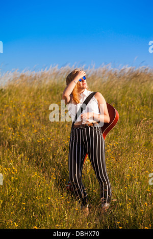 Teenager-Mädchen zu Fuß durch eine Wiese mit einer Gitarre. Im Freien. Sommer. Stockfoto