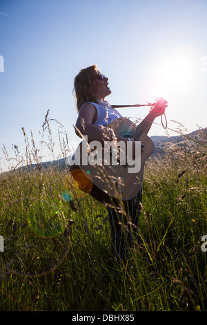 Teenager-Mädchen mit dunkler Brille Gitarre in einer Wiese. Im Freien. Sommer. Stockfoto